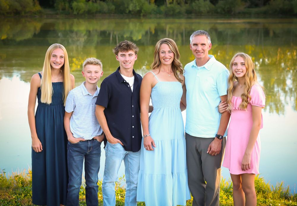 Family portrait series outdoors by a lake wearing coordinated blue and navy outfits.