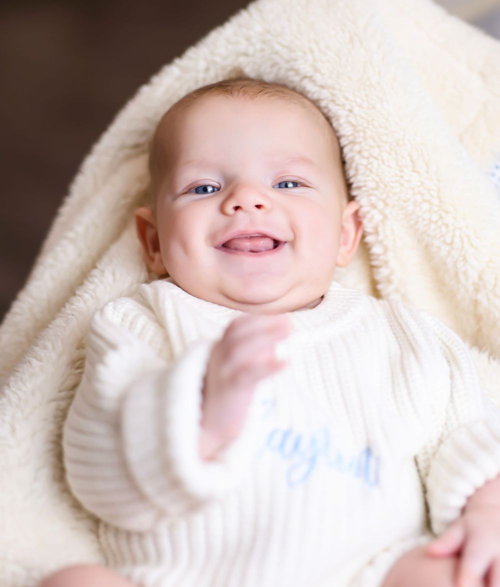 Baby wrapped in cream colored blanket smiling at camera.