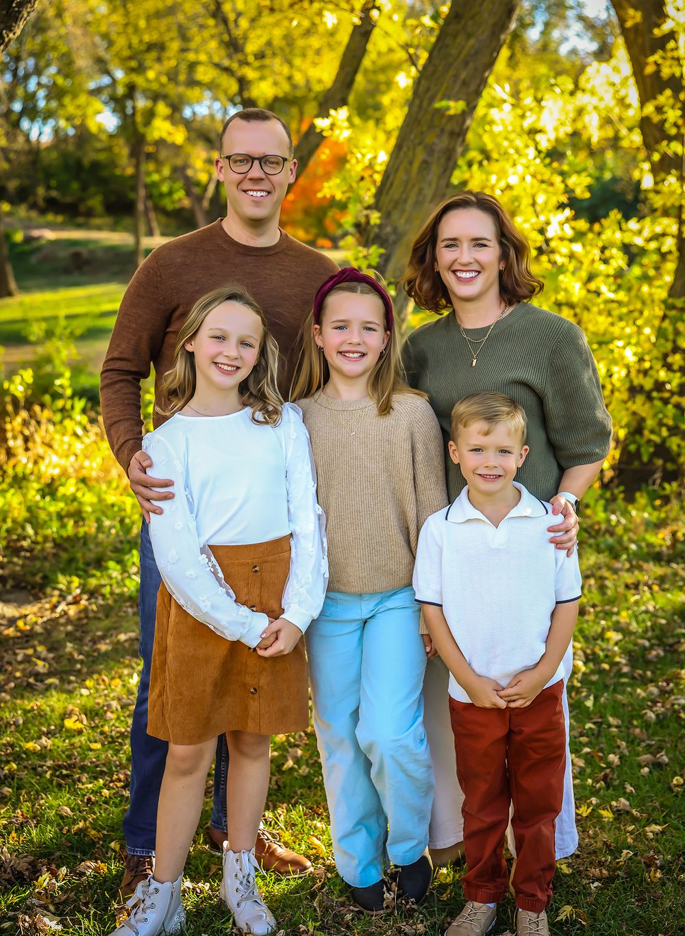 Outdoor autumn family photoshoot with golden sunlight filtering through yellow leaves in a park.