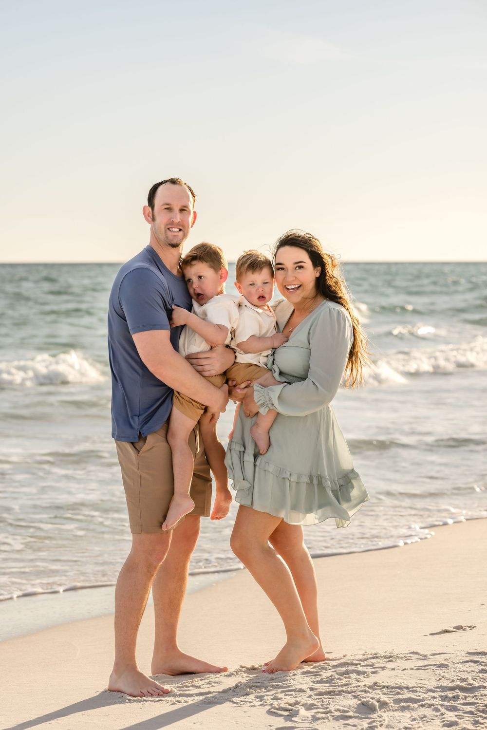 A family shares joyful moments together during a sunset photoshoot at the beach with waves in the background.