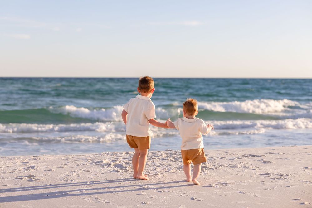 Two figures run joyfully along a white sandy beach with ocean waves in the background during sunset.