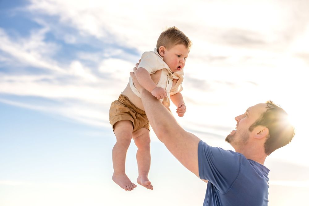 Parent and baby playing together outdoors at sunset with lens flare creating a warm, joyful atmosphere.