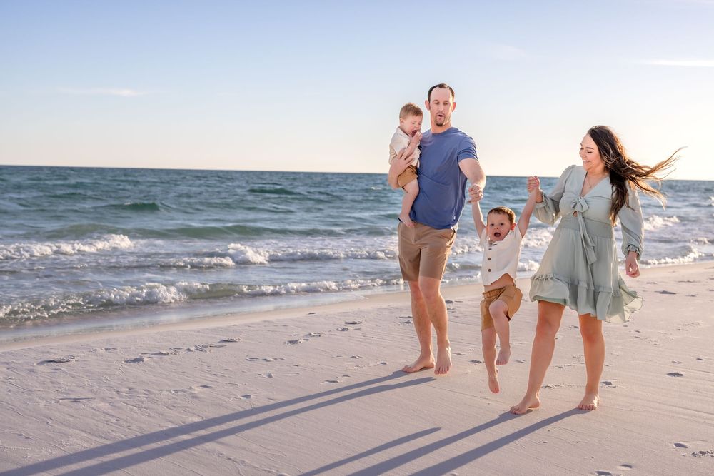 A family enjoys a playful moment together while walking along a sandy beach at sunset.