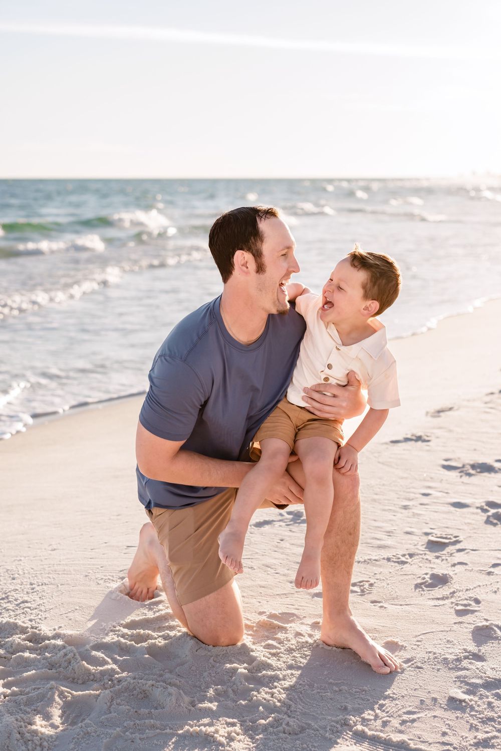 Playful beach moment captured between parent and child on white sand with ocean waves behind them.