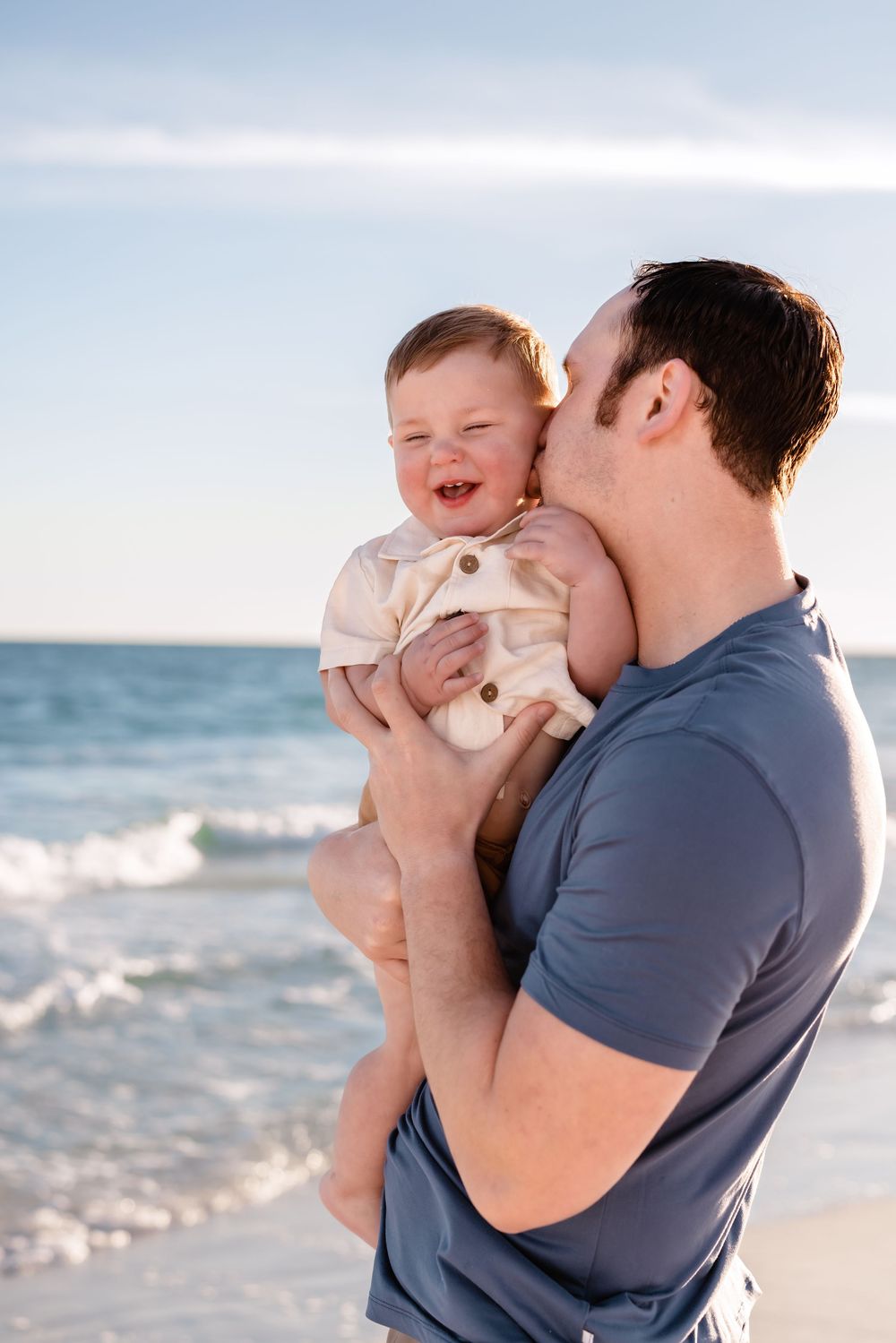 Tender family moment captured at sunset on the beach with gentle ocean waves in the background.