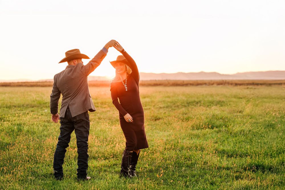 Two silhouetted figures walk through a golden field at sunset with warm sunlight illuminating the pastoral landscape.