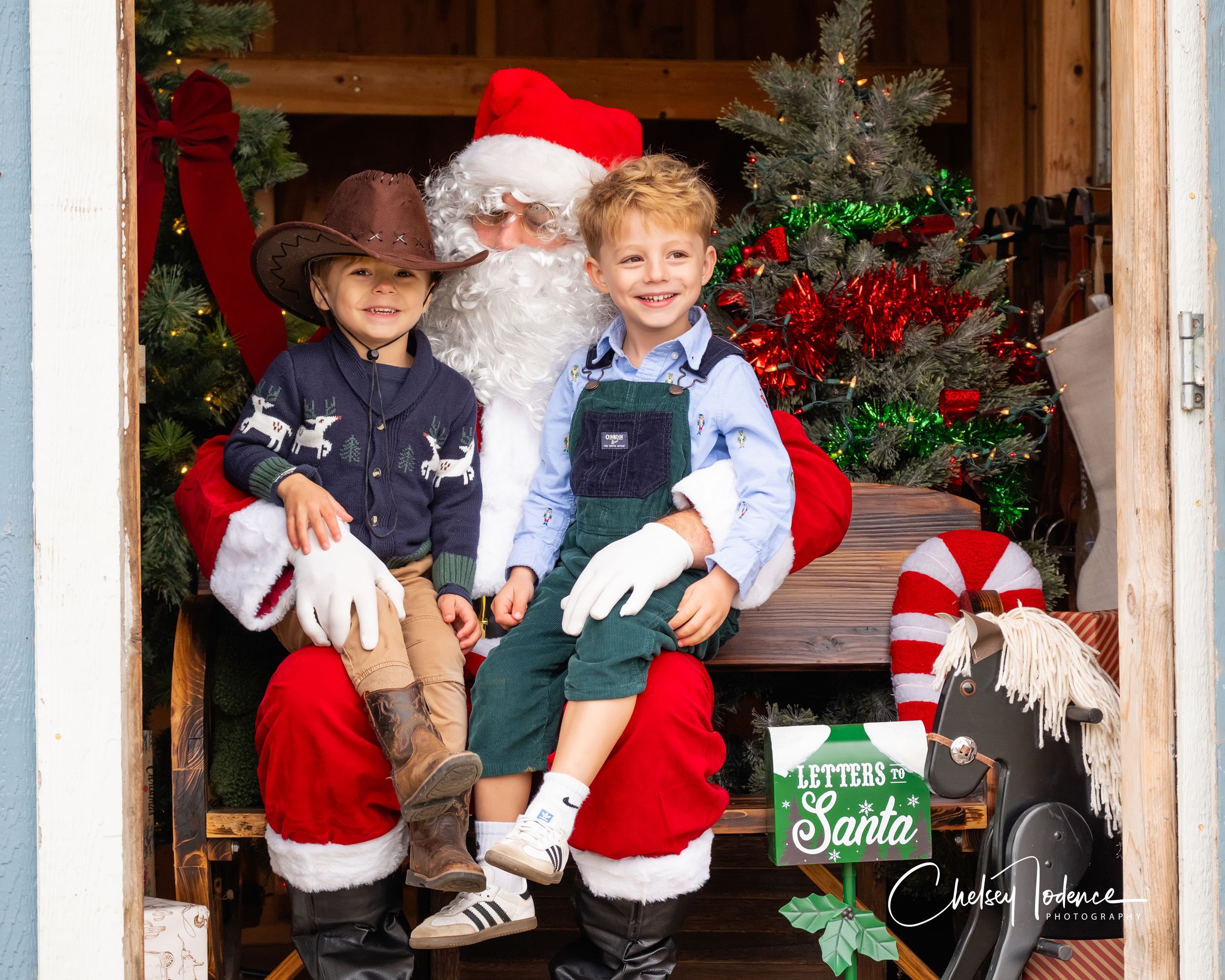 Children sitting with Santa at a rustic barn Christmas photo session in Petaluma, California, surrounded by holiday decor and farm charm