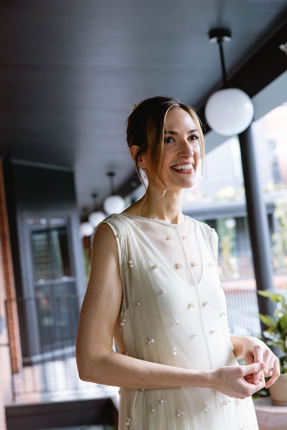 A bride in a delicate pearl-embellished dress smiles on a covered outdoor porch. Pizzeria Beddia Wedding. Fishtown Philadelphia, PA.