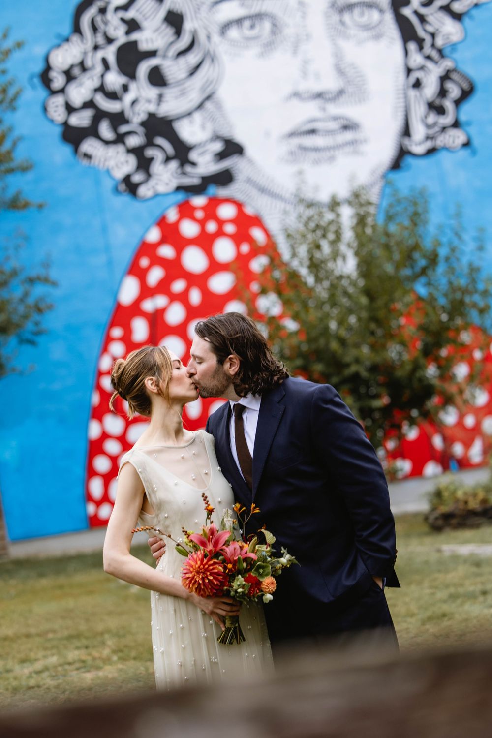 A romantic wedding portrait against a blue mural backdrop with red polka dot details. Pizzeria Beddia Wedding. Fishtown Philadelphia, PA.