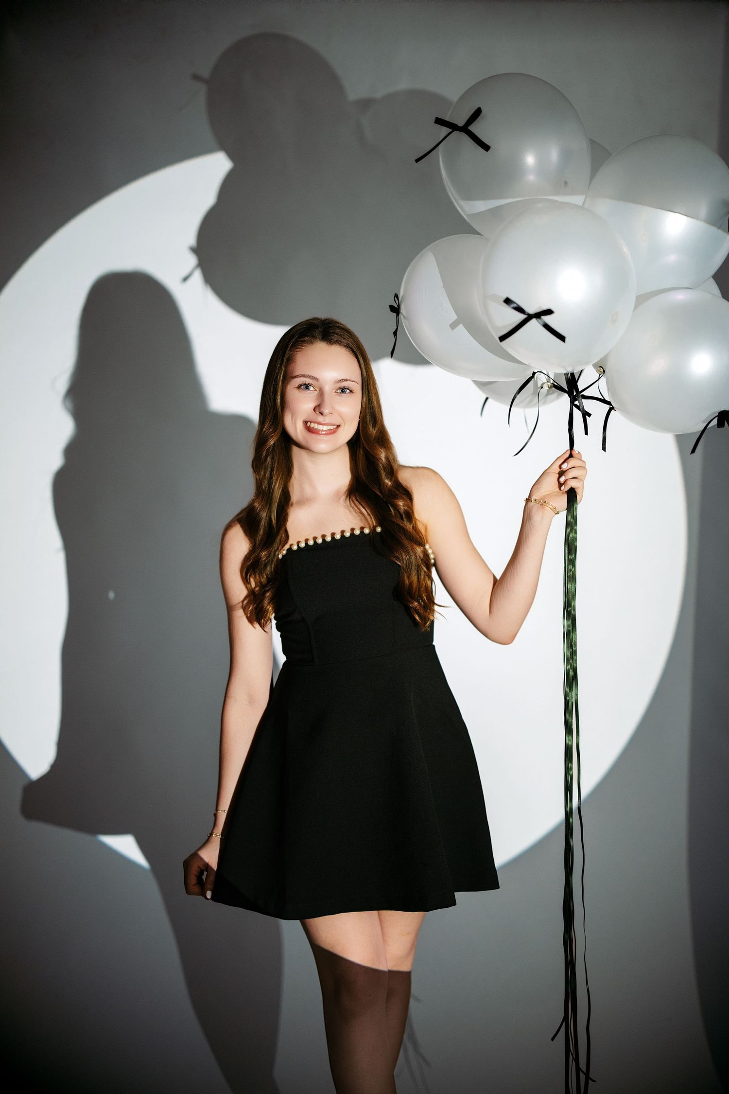 A creative photo series showing a woman in a black dress posing with white balloons against a white backdrop.