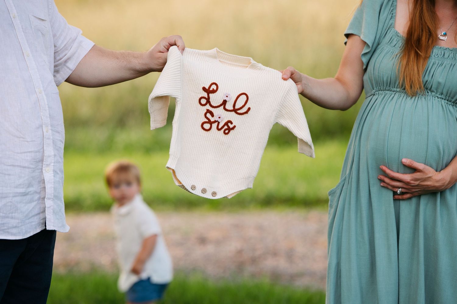 A family holds embroidered baby clothes in a sunlit outdoor setting .  Maternity photoshoot professional photographer.  Middle TN.