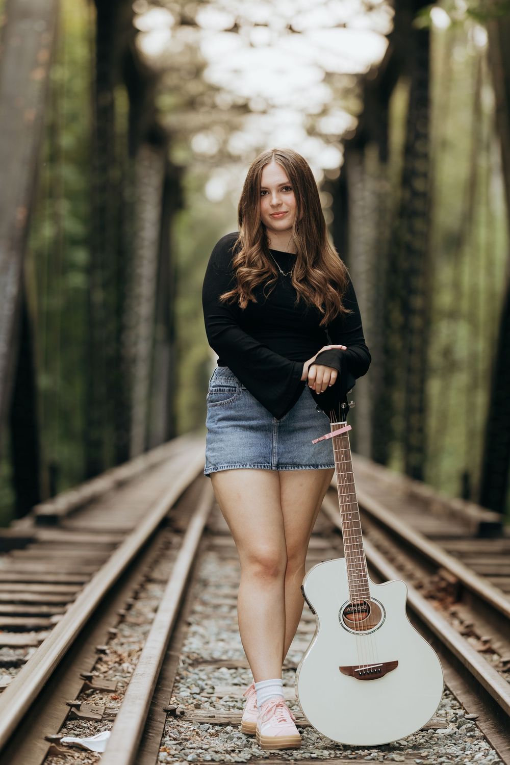 Artistic portrait with acoustic guitar on railroad tracks in forest setting.