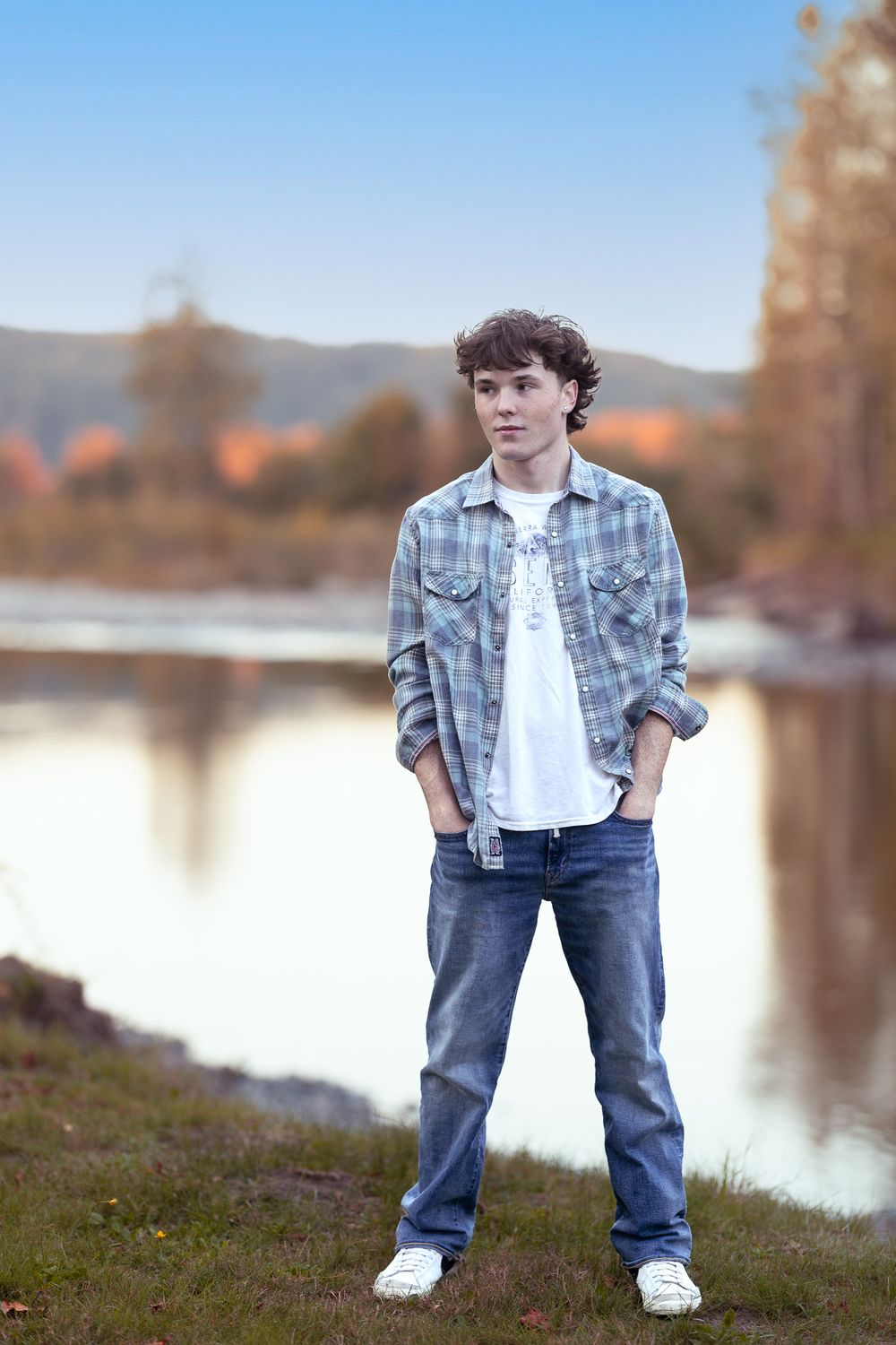 A casual portrait by a lake featuring plaid shirt and jeans against an autumn backdrop.