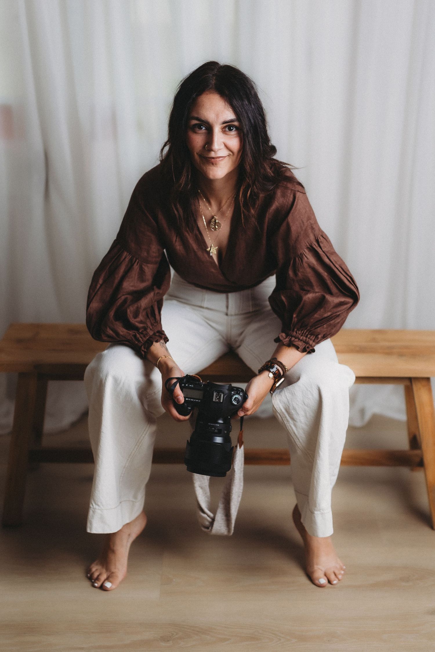 Person in brown top and white pants sitting on floor with camera in artistic photography sequence.