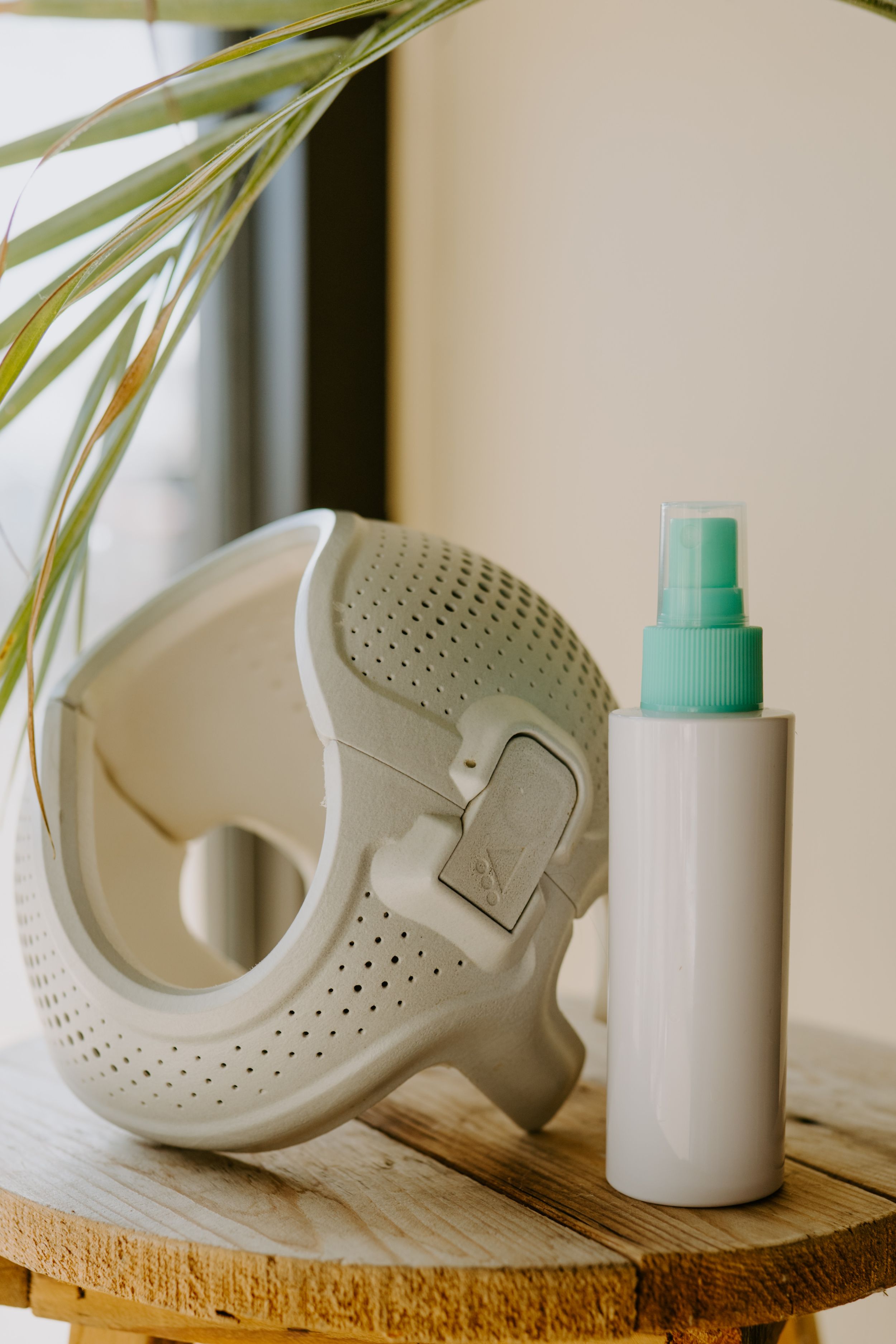 White protective mask and spray bottle displayed on wooden surface with plant in background.