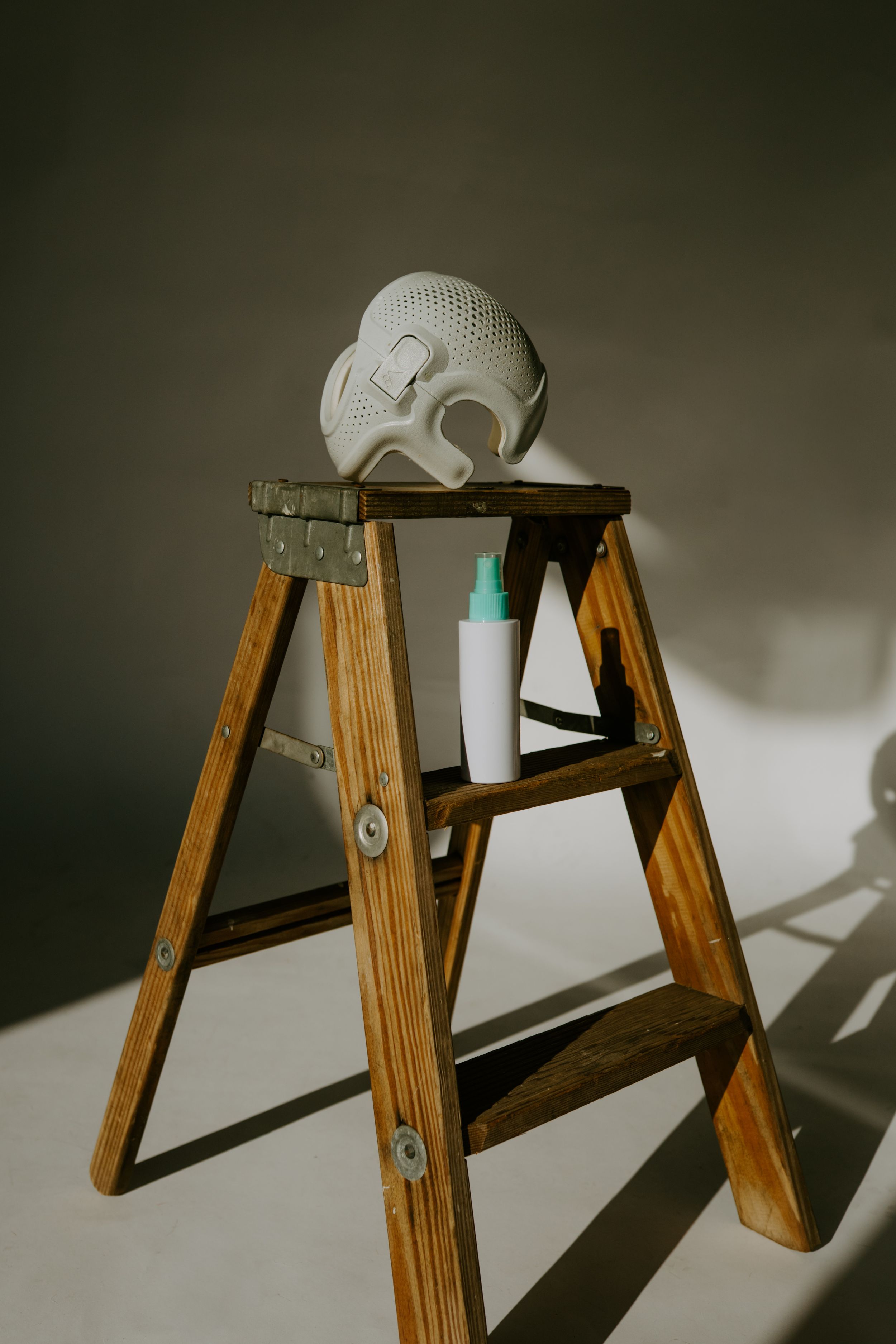 Wooden step ladder with white protective mask and spray bottle in dramatic lighting.