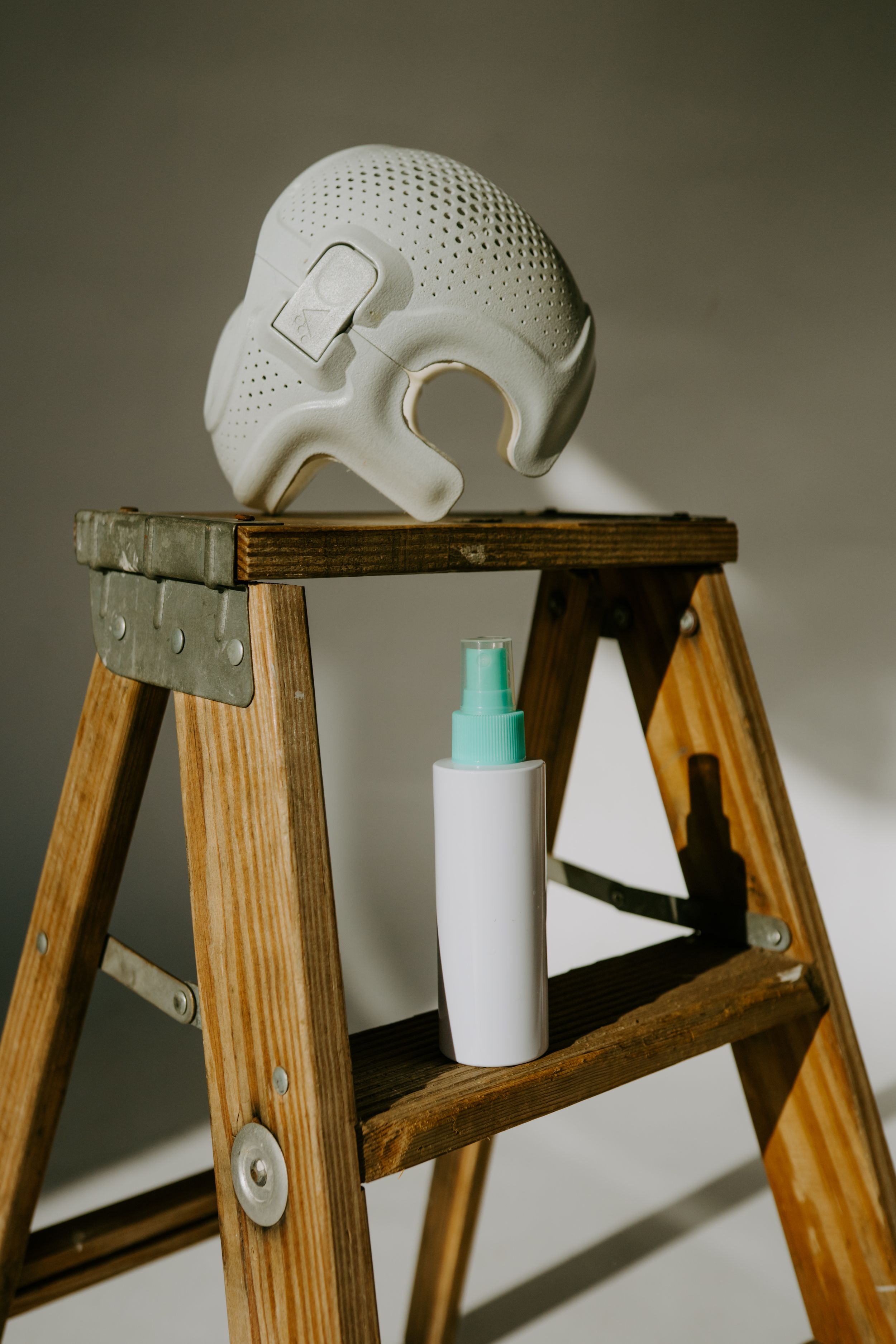 White perforated helmet and spray bottle arranged on vintage wooden ladder.