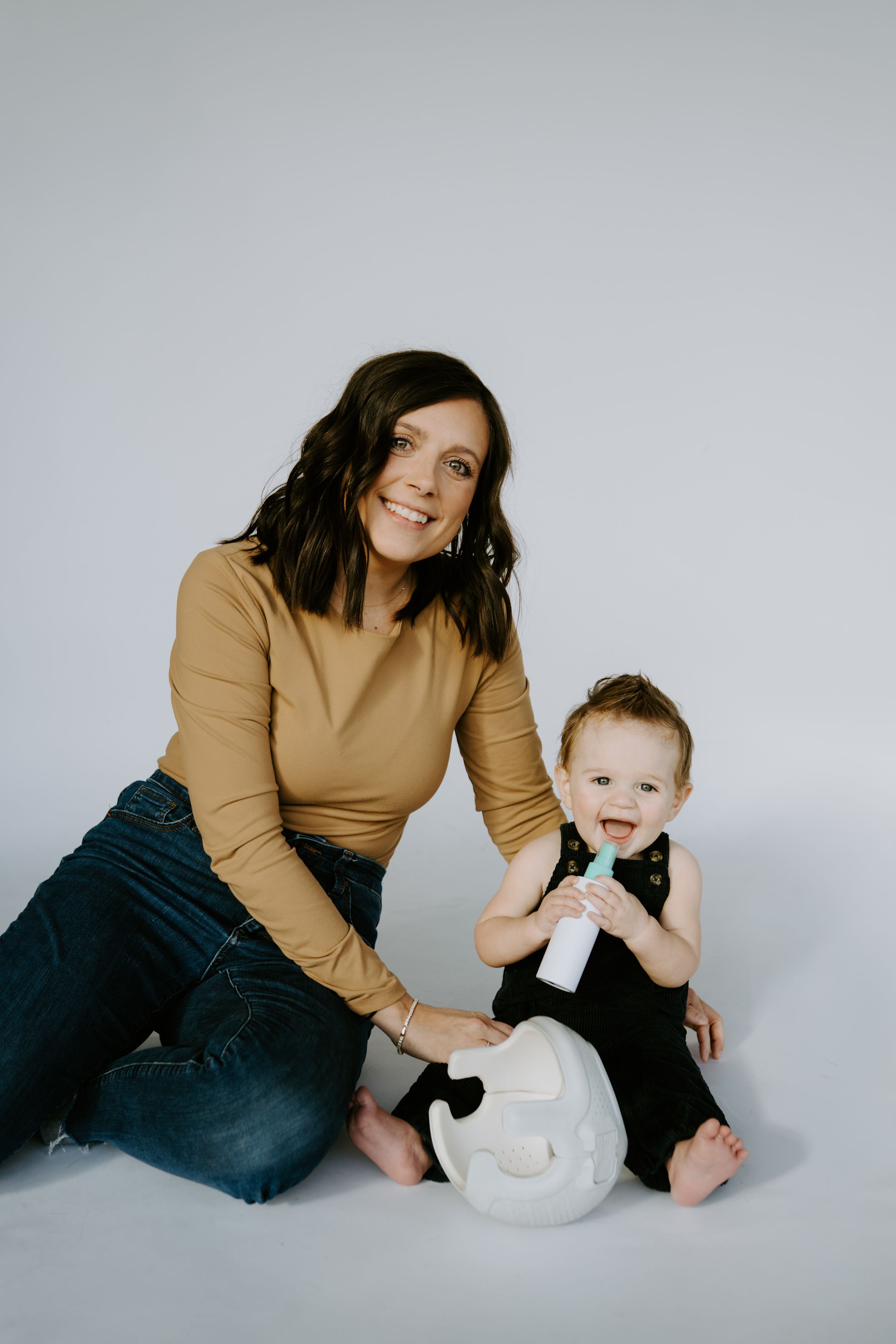 Woman in tan sweater and jeans sitting with child next to white helmet on floor.