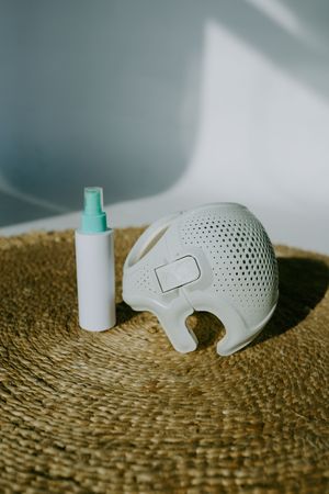 White perforated helmet and spray bottle displayed on woven jute rug.