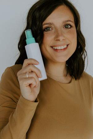Woman in tan sweater holding white spray bottle with turquoise cap.