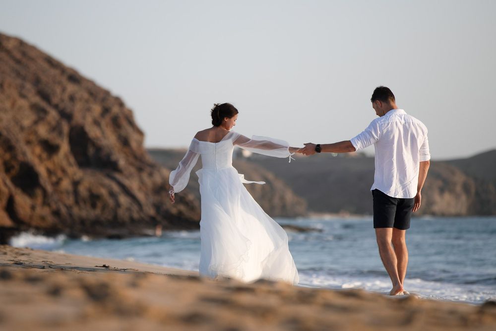 Newlyweds walking hand-in-hand along the golden shore of Papagayo beach - Lanzarote wedding photographer