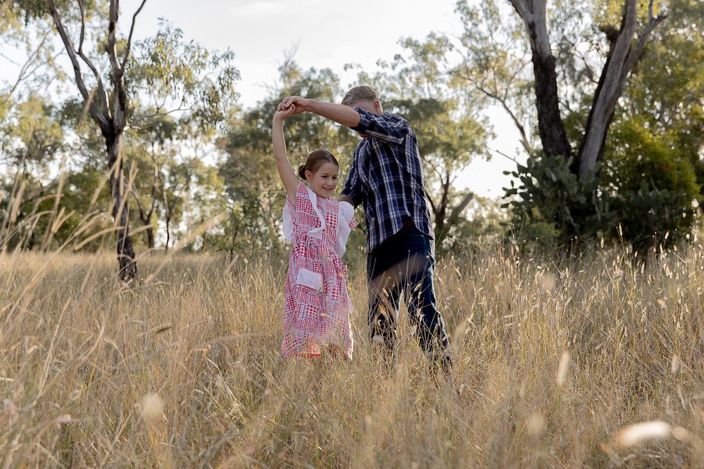 father twirling daughter around in a field during a professional family photo shoot.