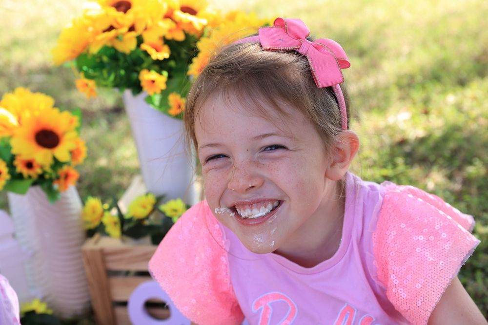 little girl eating cake and laughing  during a professional sunflower outdoor cake smash photo shoot.