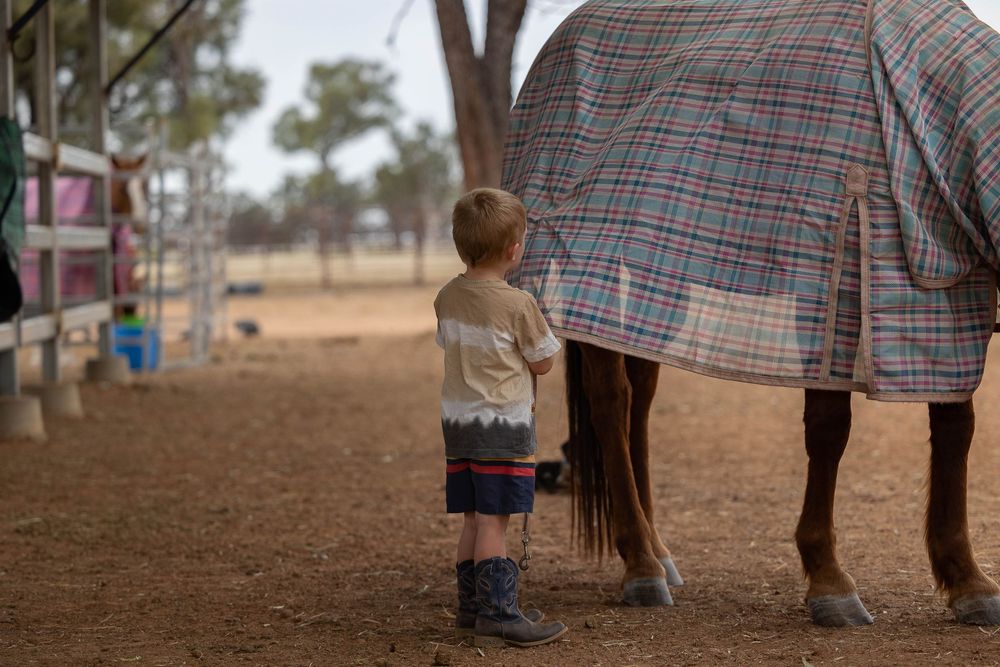 little boy doing up the leg straps while rugging his horse