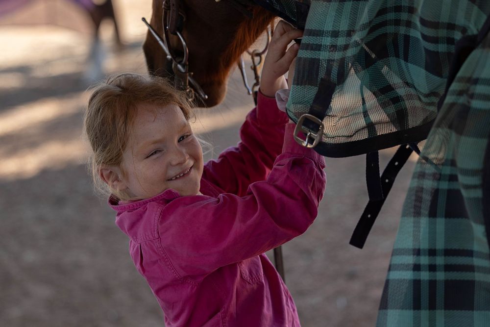 little girl doing up the neck straps while rugging her horse
