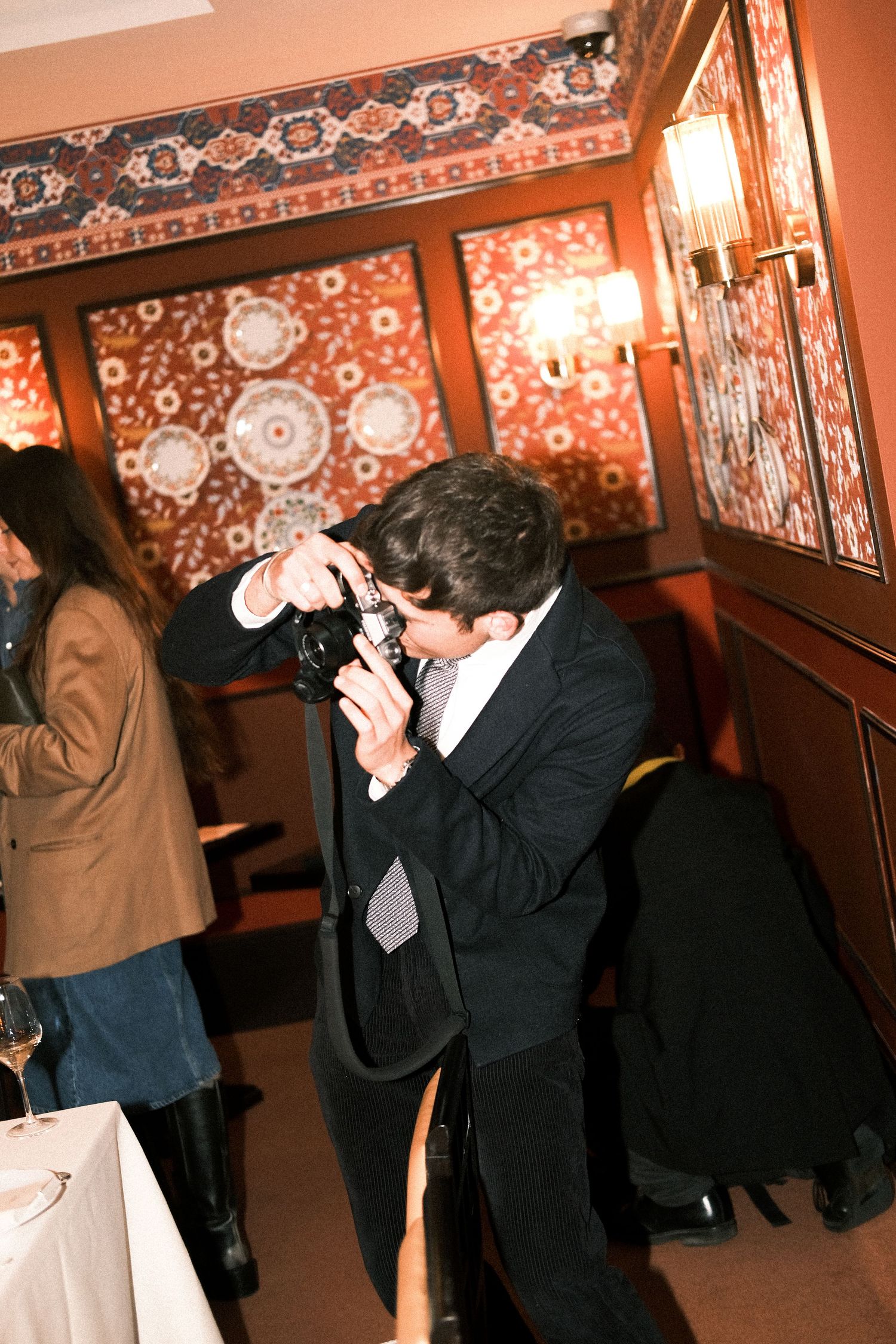 Photographer taking candid shots at an indoor event with decorative wallpaper and warm lighting.