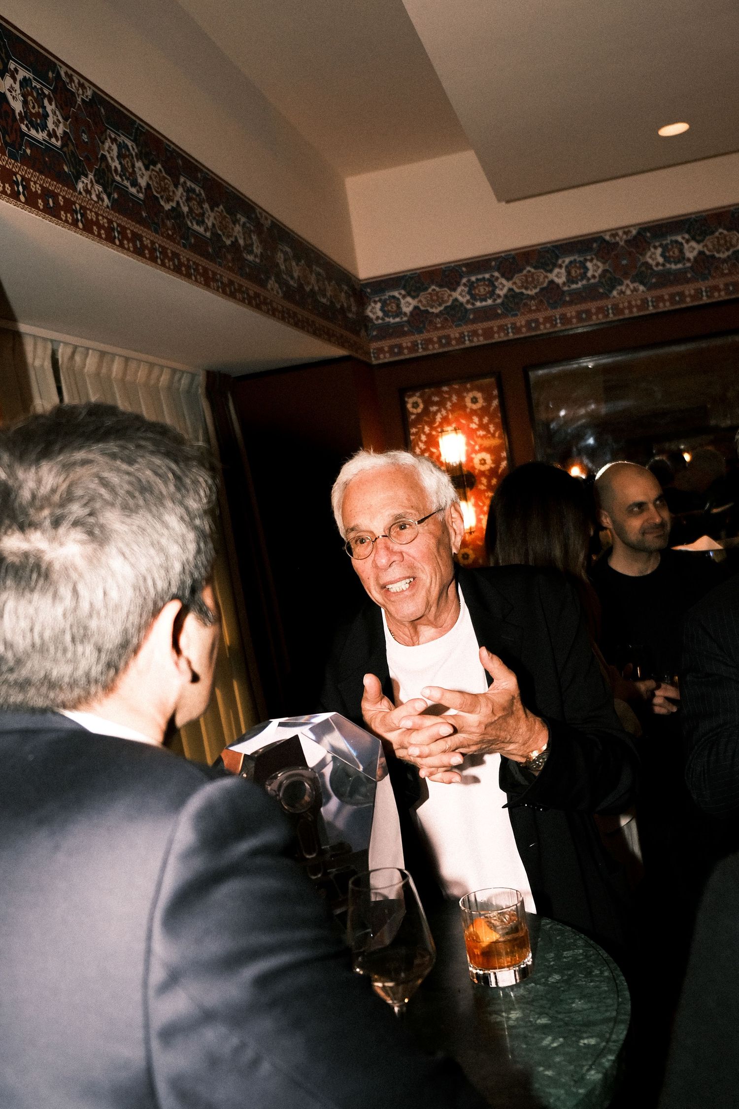 People socializing and laughing together at an indoor gathering with dim lighting and decorative borders on the walls.