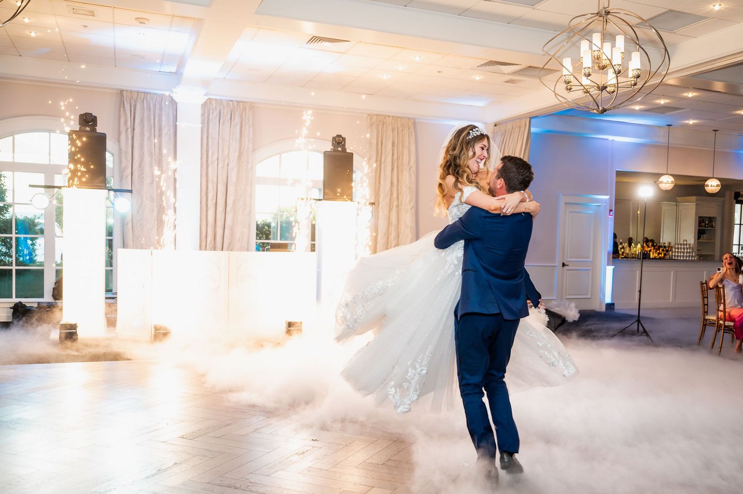 A grand ballroom decorated for a wedding reception with elegant chandeliers and flowing white decor.