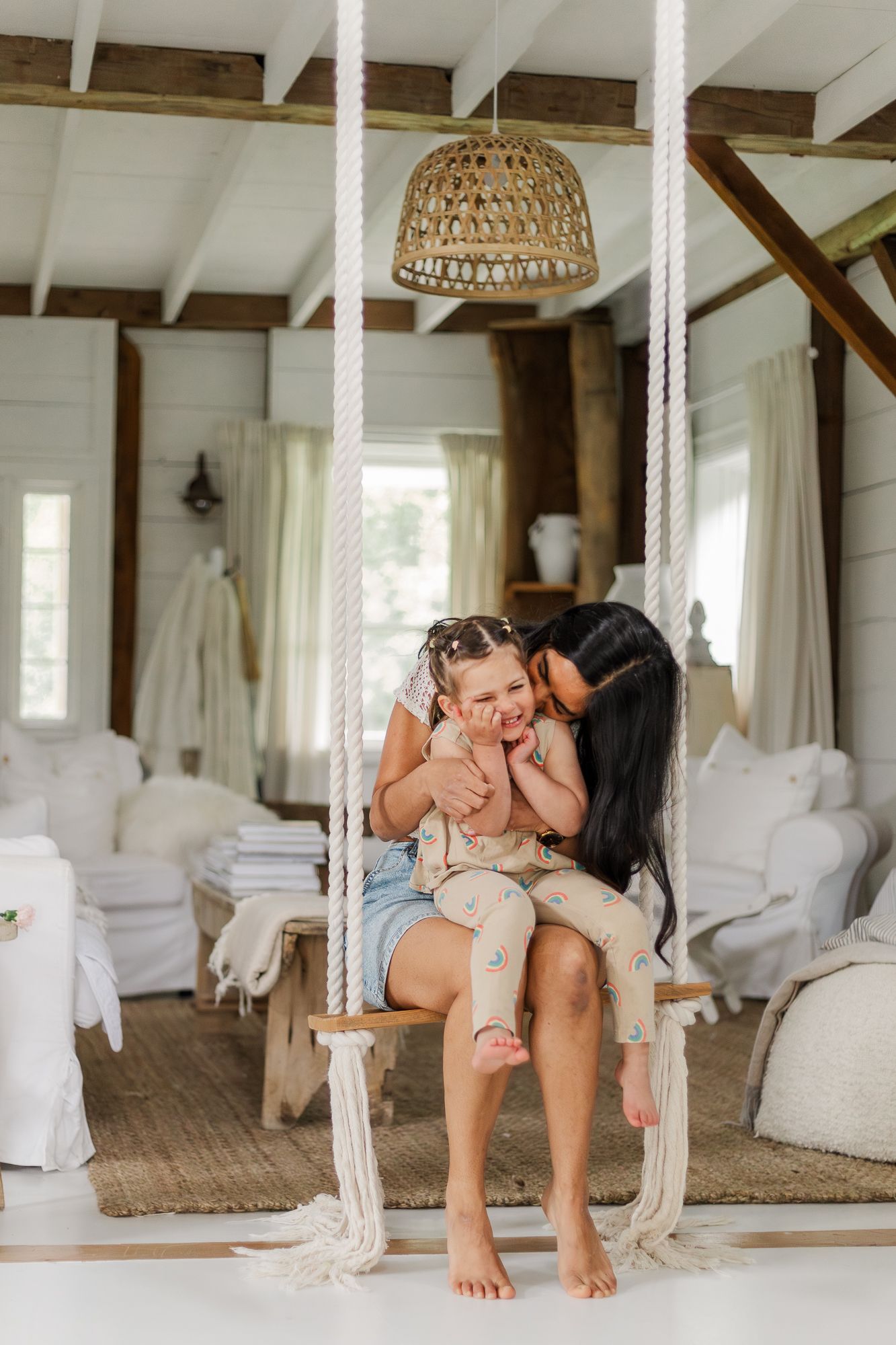 A mother sitting with her daughter on a cozy indoor swing decorated with macrame inside the white countryside house in waterford ontario.