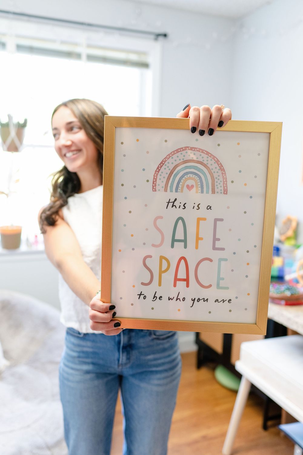 Person holding colorful rainbow safe space sign in bright interior room.