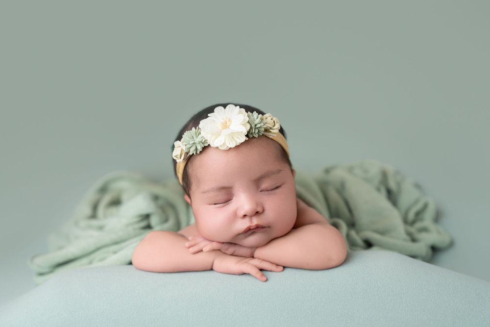 Newborn baby sleeping peacefully on mint green blanket with white floral headband.