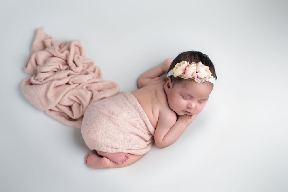 A series of minimalist newborn photos showing a sleeping baby wrapped in soft pink fabric against a white backdrop.