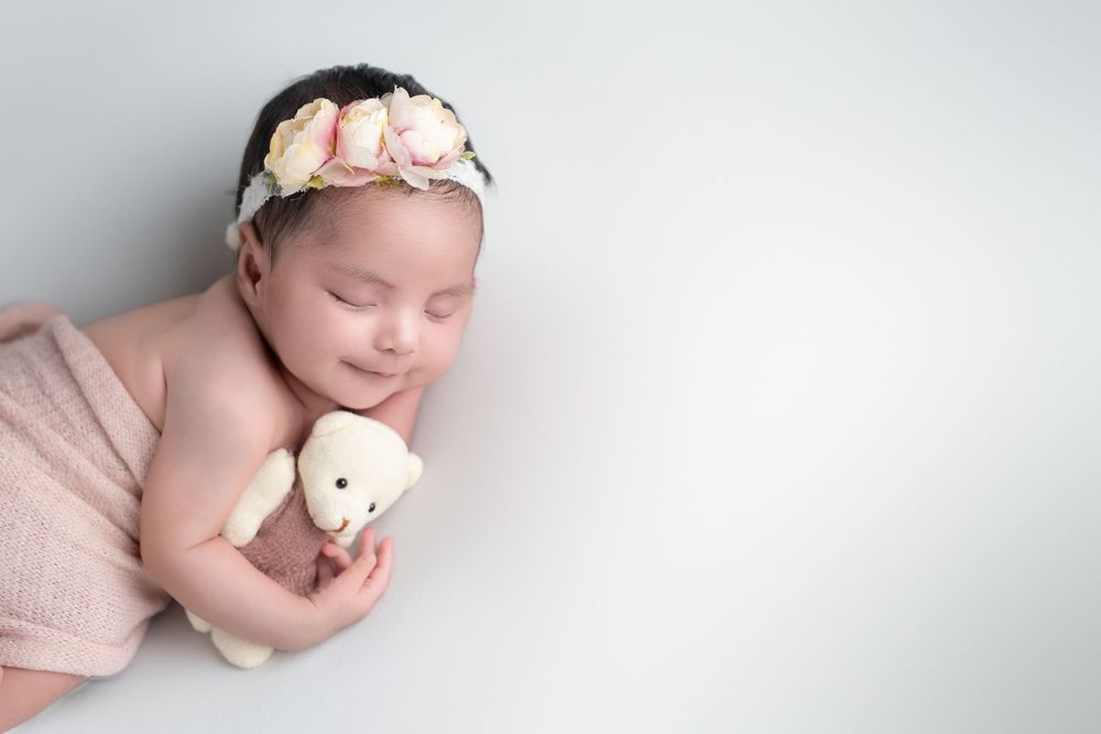 Sleeping newborn baby in soft pink tones lies peacefully on white blanket during professional photo session.