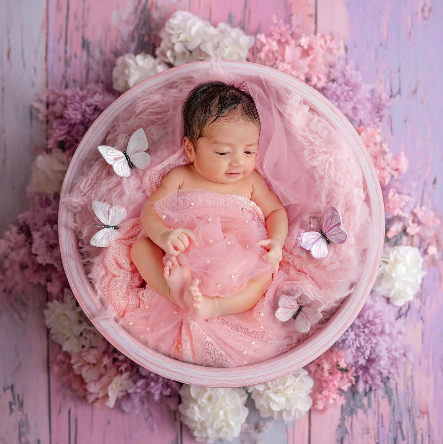 Newborn photography series in pink with delicate butterflies and floral decorations on a soft textured backdrop.