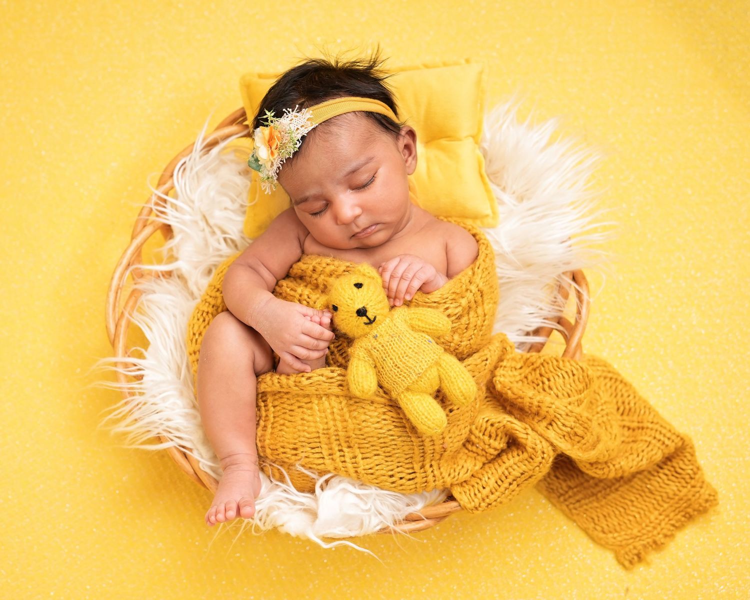 A sleeping baby in a yellow knit outfit cuddles with a plush toy on a cozy white blanket.