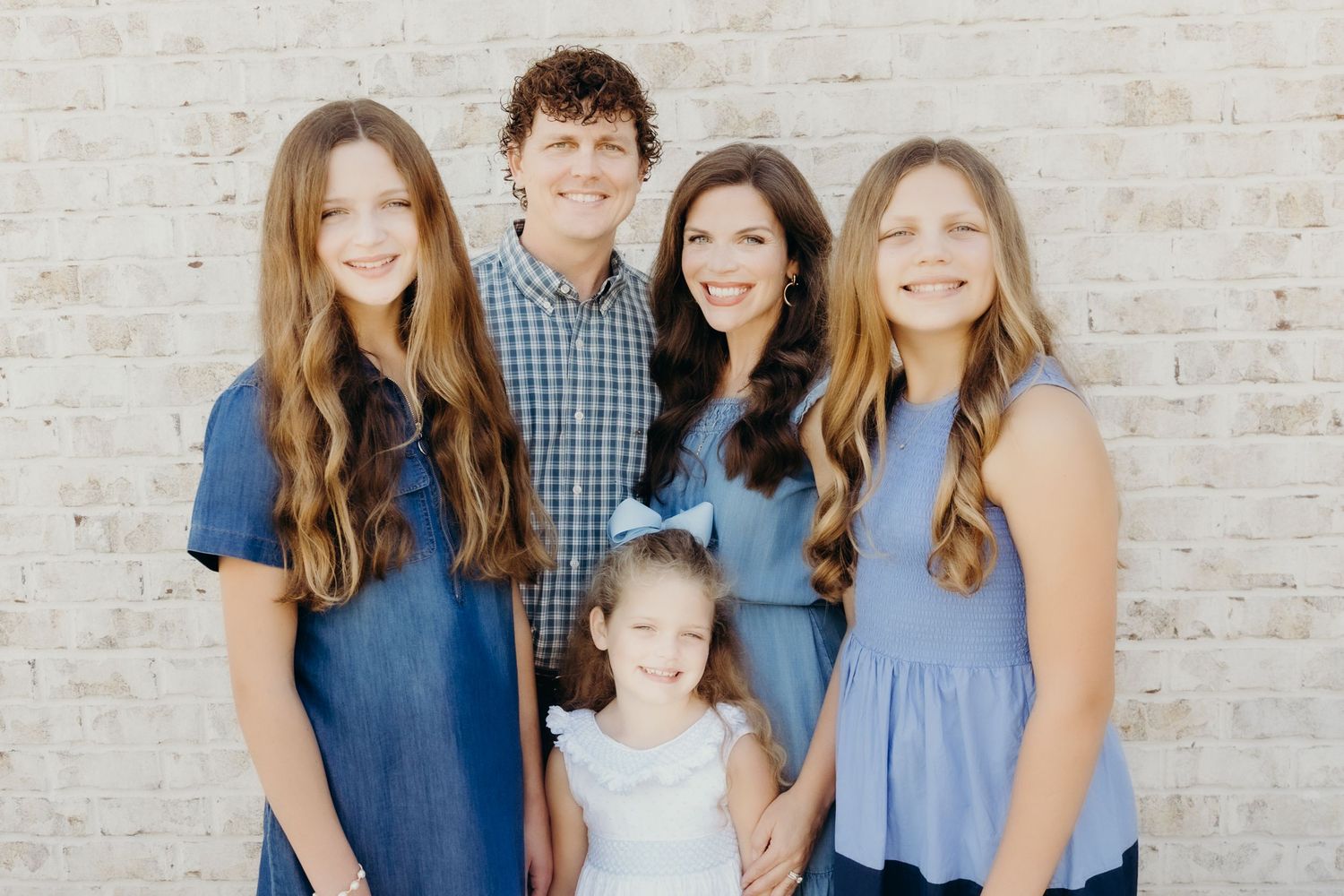 A family group in coordinating blue outfits poses together against a brick wall.