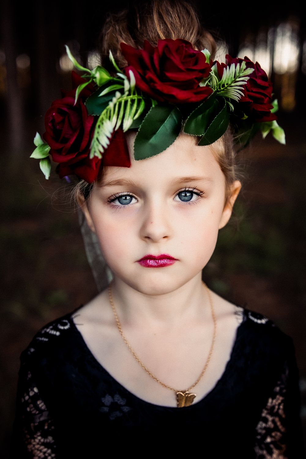 Close-up portrait wearing a floral crown with red roses against dark background.