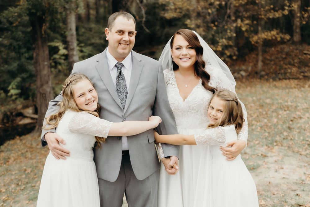 Wedding party poses together outdoors during autumn with fallen leaves in background.