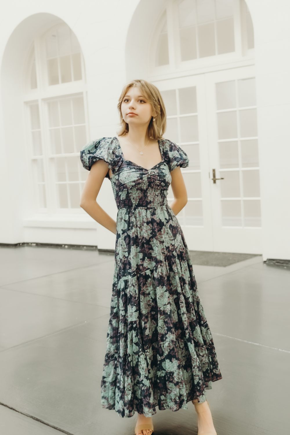 Child wearing floral print dress poses gracefully in bright white studio space.