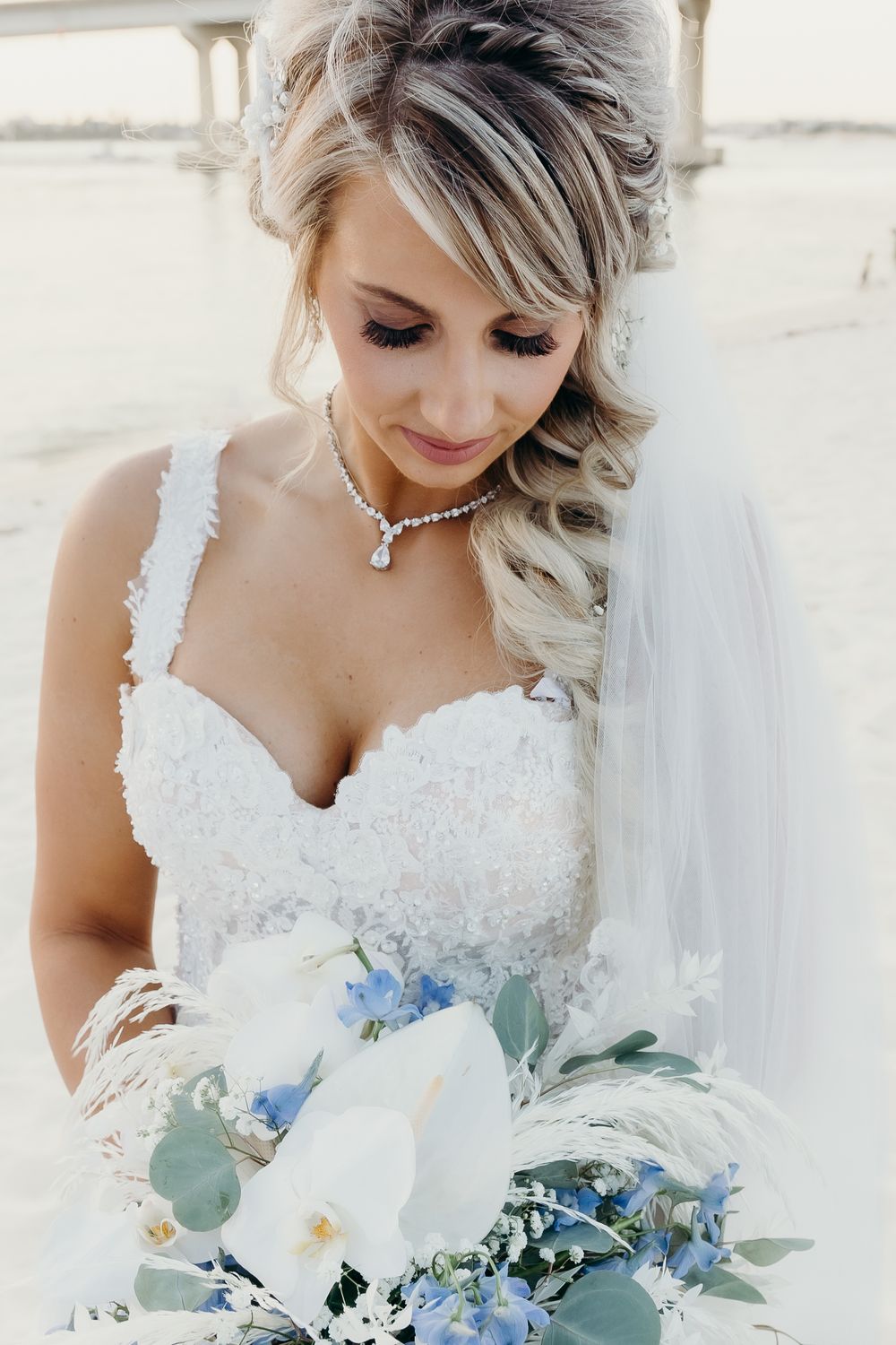A bridal portrait showing a white lace dress and blue and white floral bouquet.