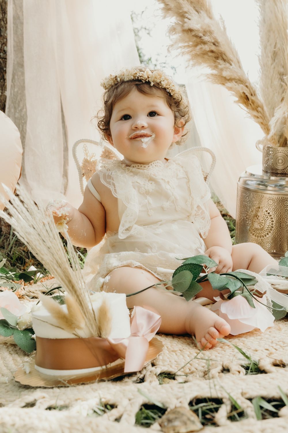 Baby in white lace dress posed with dried pampas grass and floral decorations.