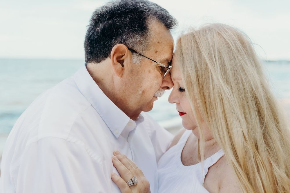 A tender moment between a couple on the beach wearing white clothing.