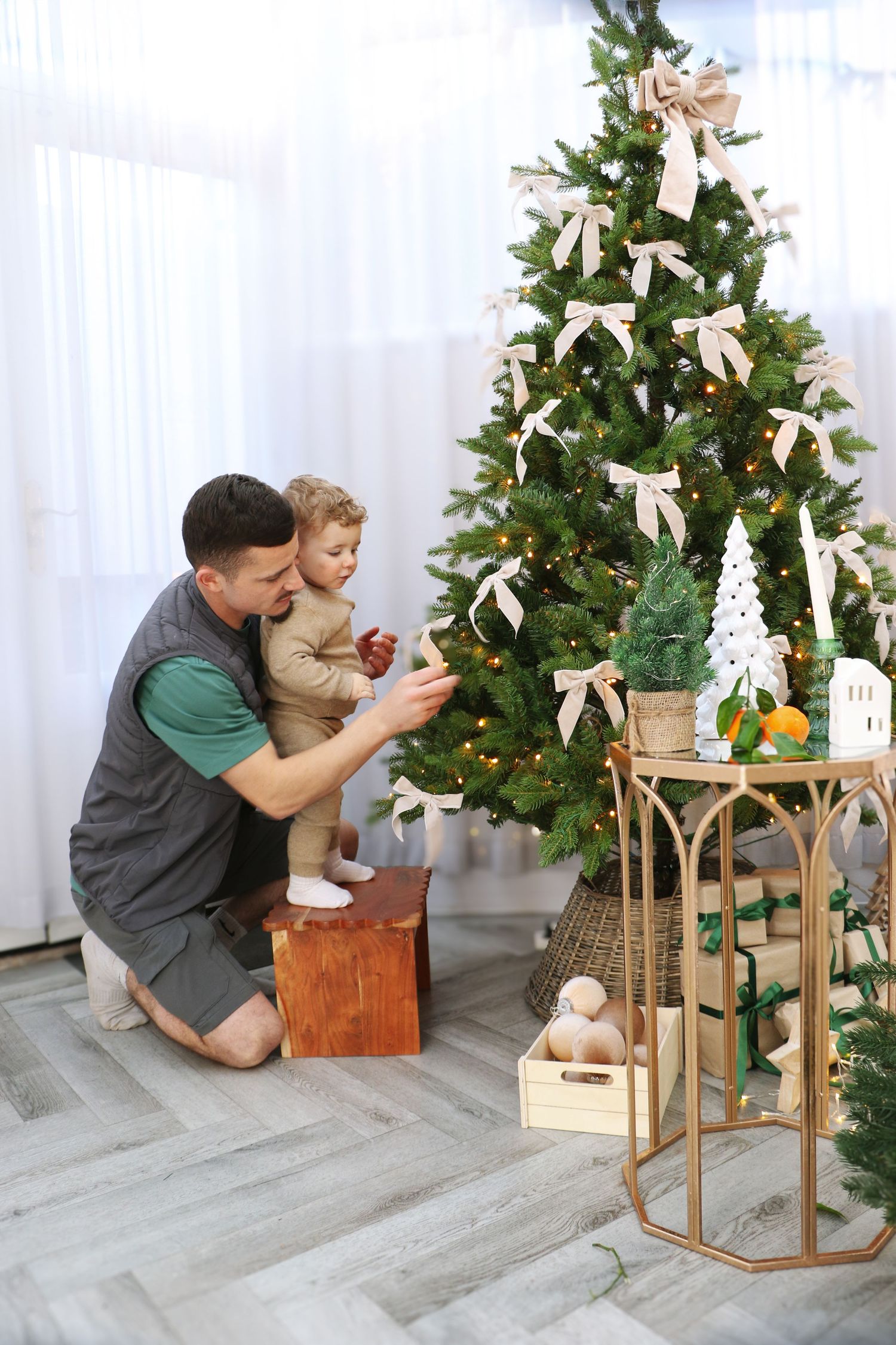 Beautifully decorated Christmas tree with white bows stands beside a decorative stand with holiday ornaments and citrus fruits.