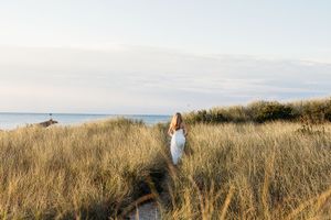 A panoramic view of a couple walking through tall grass on a coastal dune during golden hour.