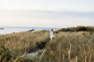 A person walks through tall grass on a coastal hillside overlooking the ocean on a cloudy day.