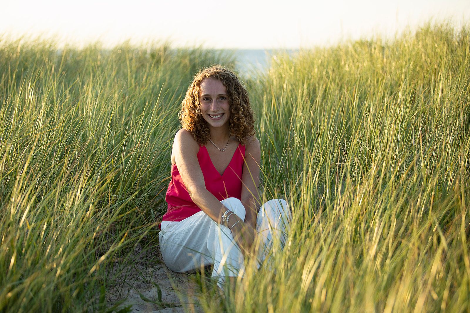 A series of seven photos showing someone in a red dress sitting in tall golden grass at sunset.